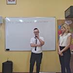 Uczeń mówi wiersz do mikrofonu. Obok stoi nauczycielka.