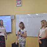 Uczennica mówi wiersz do mikrofonu. Obok stoją nauczycielki.