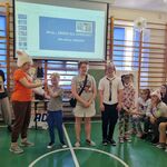 Grupa uczniów  w czapkach przedstawiających zwierzęta na tle slajdu wyświetlanego na ekranie.