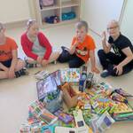 Na podłodze leżą gry, puzzle, słodycze, mazaki, zabawki. Dzieci siedzą wokół zebranych darów.
