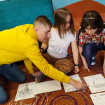 Uczniowie siedzą na podłodze, przeglądają karty pracy