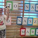 Uczennica stoi na tle drabinek z napisem ,,To nasz świat, nasze marzenia
